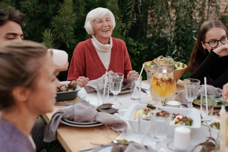 older woman smiling and laughing at dinner discussing the differences between All-on-4 vs. overdentures